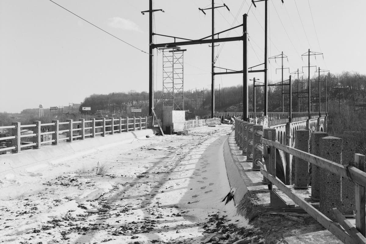 The bridge deck after the trains: snow on the empty trackbed between concrete railings, under the old catenary.