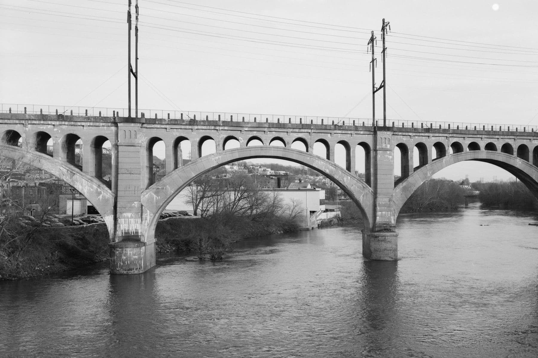 The Manayunk Bridge from the north bank of the Schuylkill: three concrete arches on stone-faced piers, with small arches under the deck.