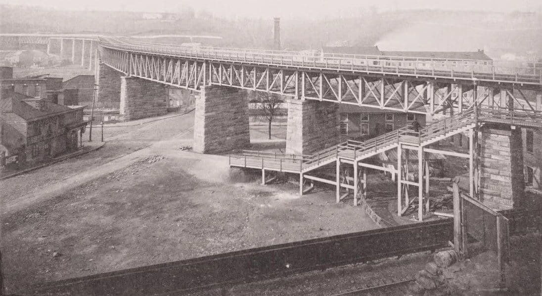 The 1884 S Bridge: iron deck trusses on tall stone piers curving across the valley, with a timber stair in the foreground.